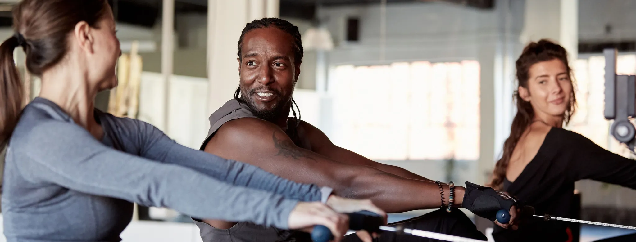two women and one man on rowing machine at gym